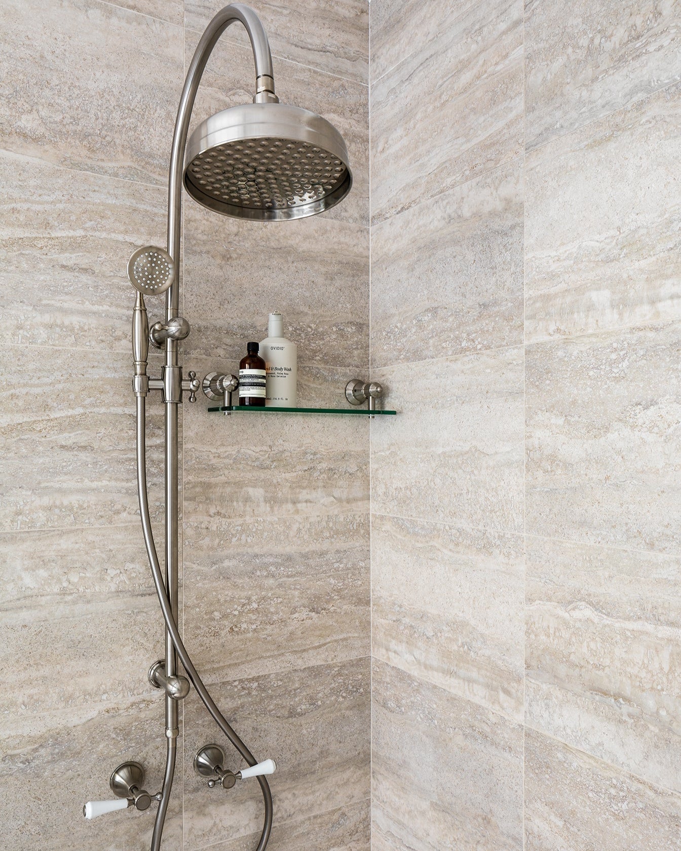 Traditional shower fixtures on travertine tiled wall.